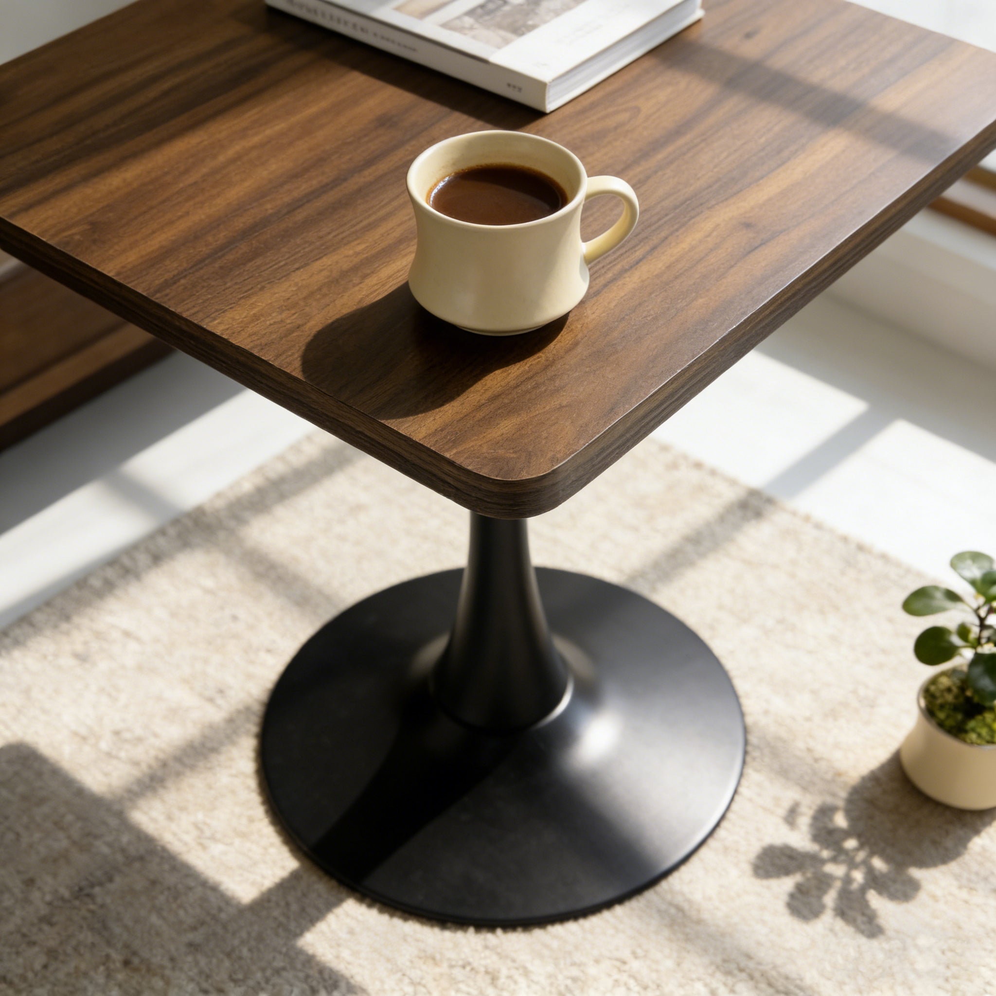 Close-up angled view of the walnut tabletop and black tulip base with a coffee mug in sunlight