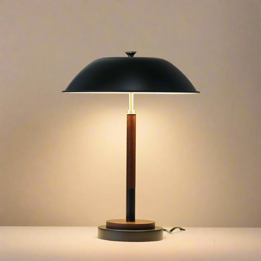 closeup of a black table lamp in mid century modern style with a wood stem and gold accents the lamp is on showing warm light