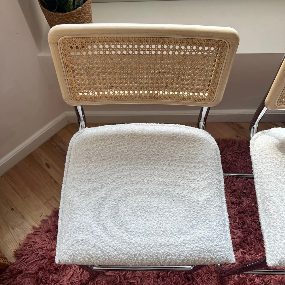 Midcentury Modern Counter Stools Set of 2 with white bouclé seats, rattan backs, and stainless steel legs on a hardwood floor.