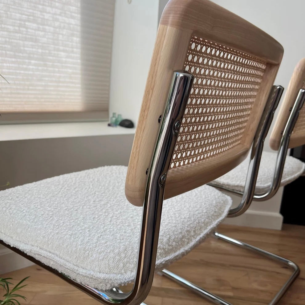 closeup of solid wood backrest with rattan accents attached to the stainless steel frame of a mcm dining chair with white boucle seat
