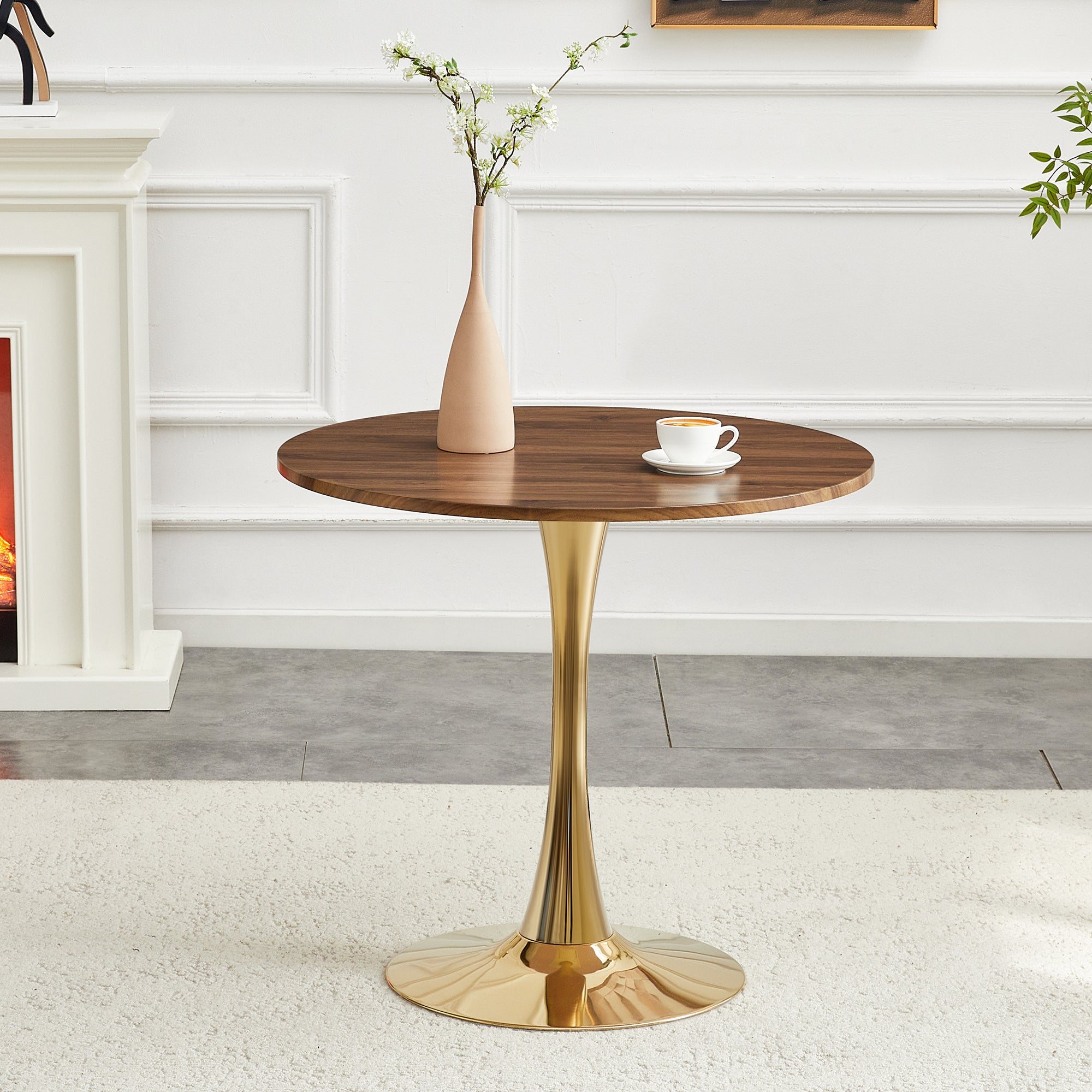 Walnut-top gold-base dining table beside a lit fireplace with a vase and coffee cup, angled view