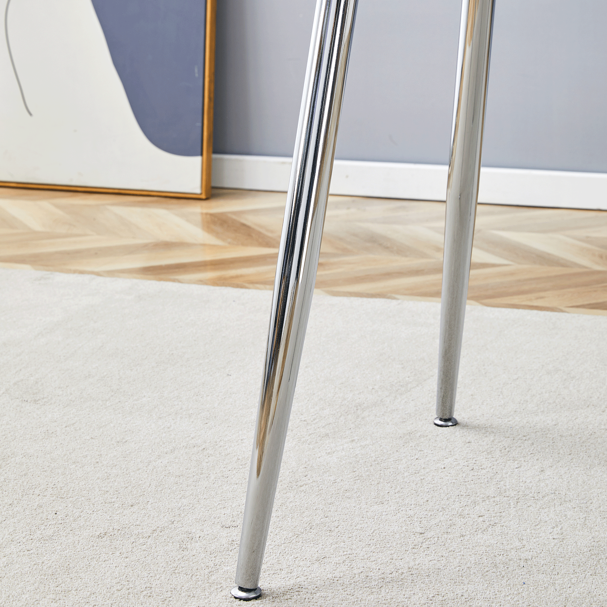 Close-up of the chrome tapered legs of the glass dining table on carpet by a wall