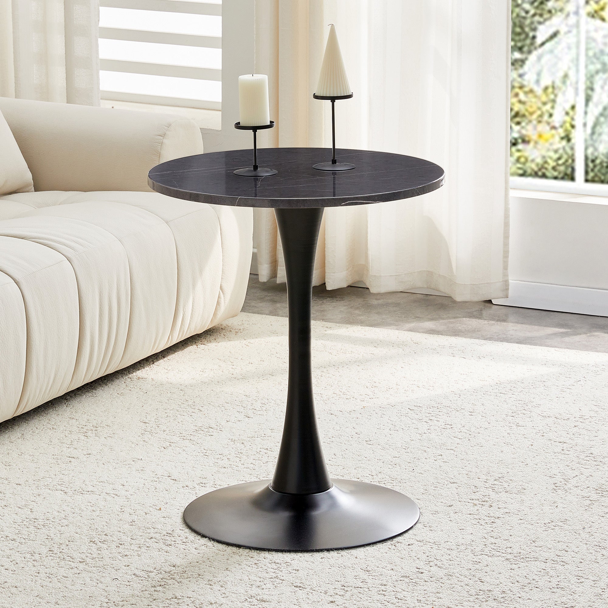 Black marble-look bistro table holding a candle and cone candle by a cream sofa, three-quarter view