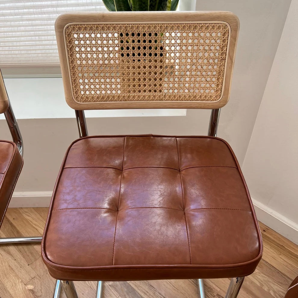 closeup of brown vegan leather seat on a mid century modern counter height bar stool with a solid wood back and rattan accents