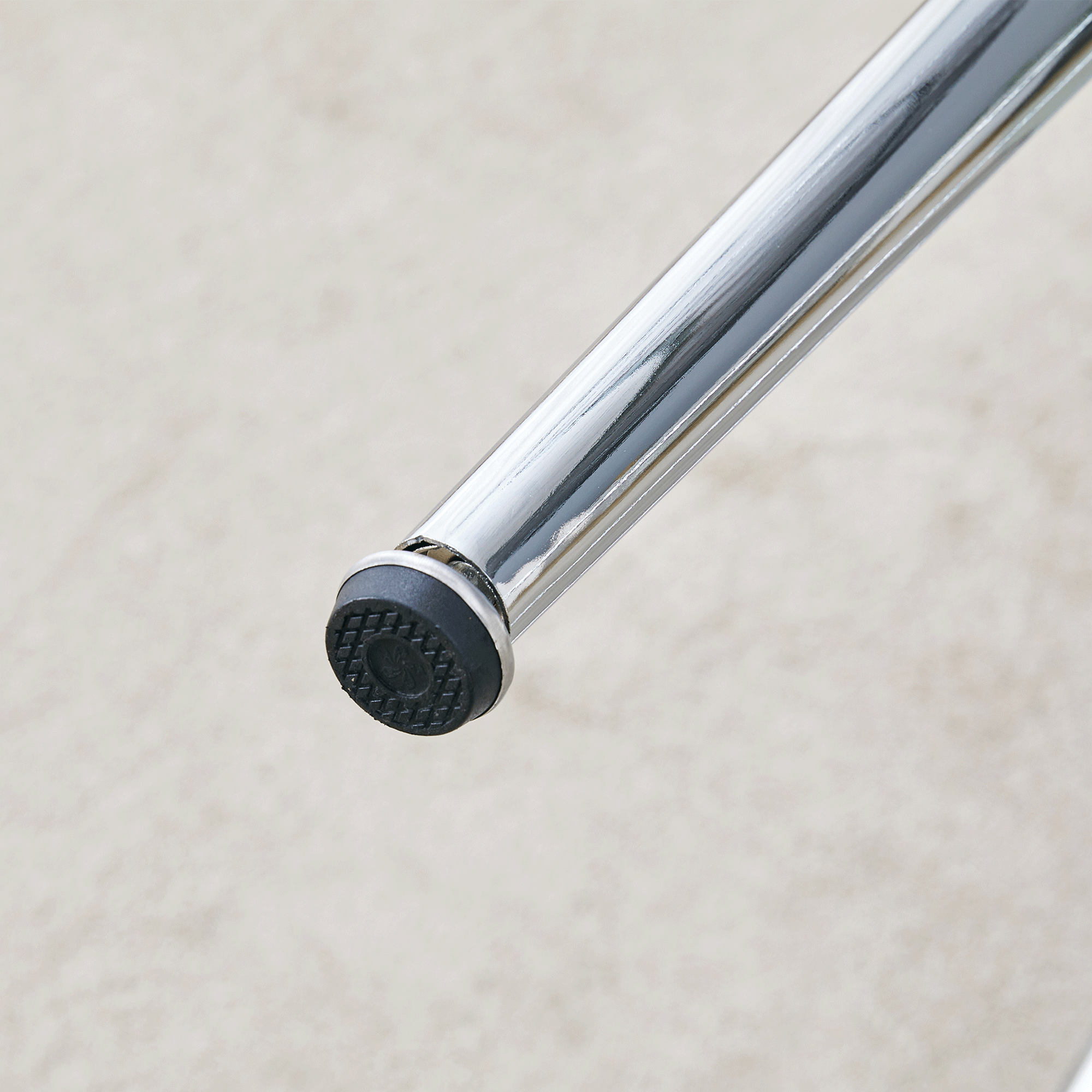 Close-up of a chrome leg foot with a black non-slip pad resting on carpet