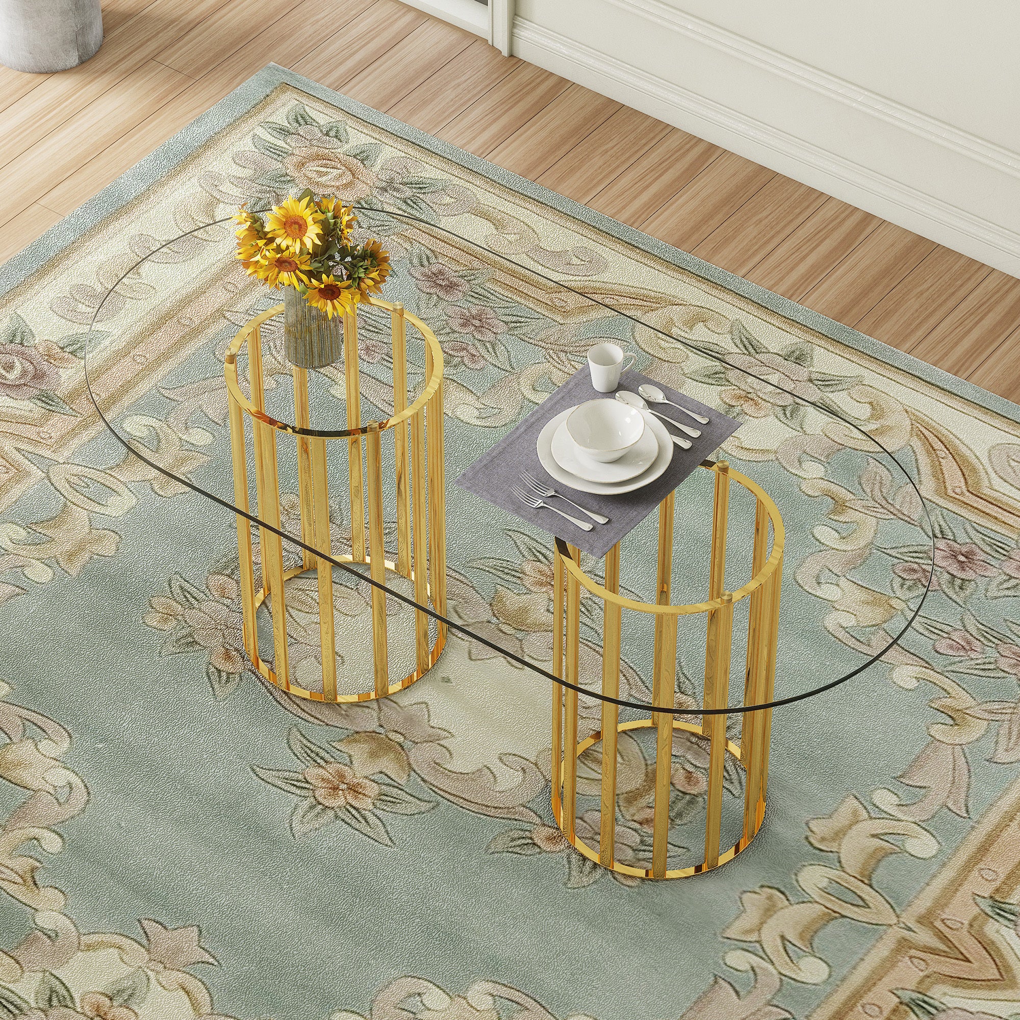 Overhead view of oval glass dining table with gold double-column base, set with dishes and sunflowers on a floral rug