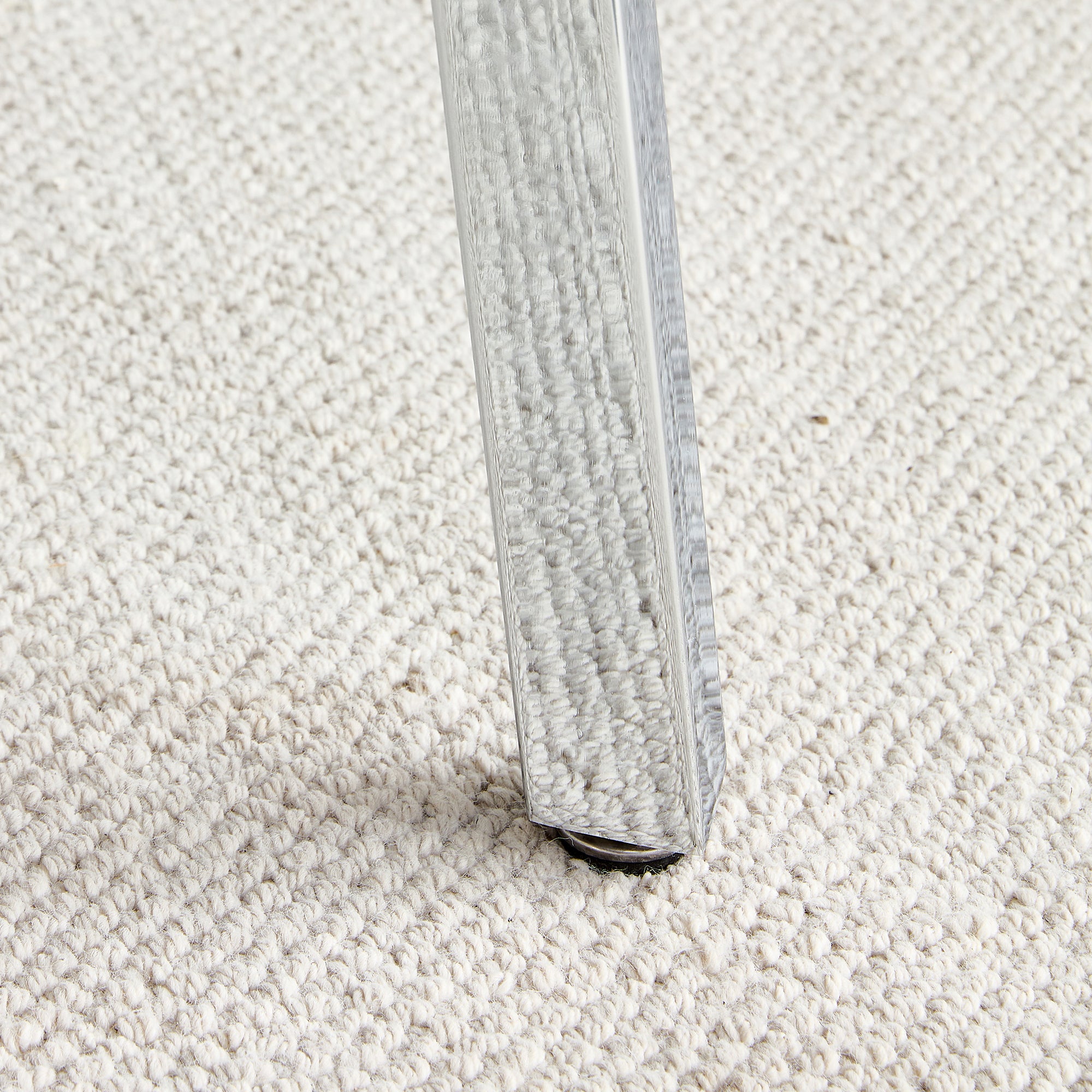 Close-up of a chrome table leg foot resting on cream carpet