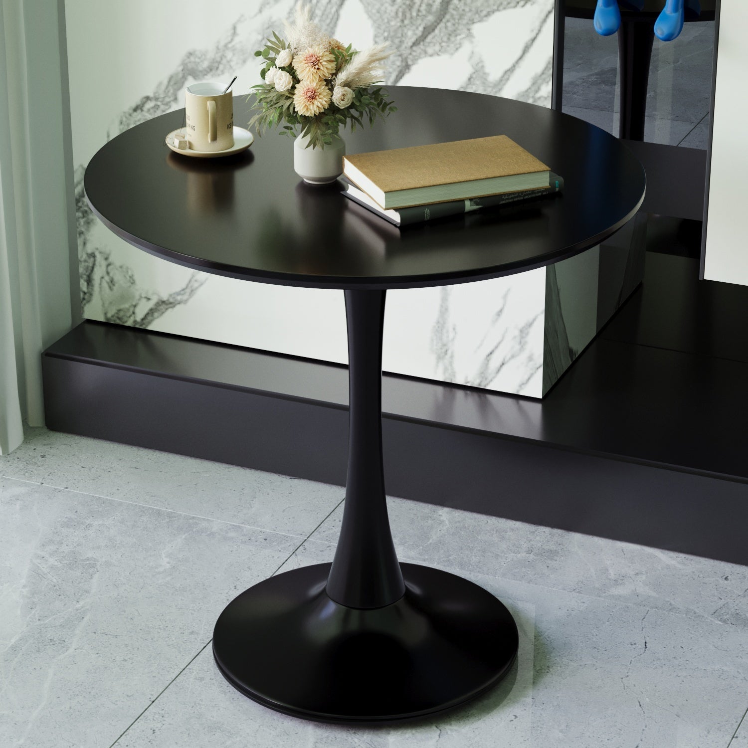 Black round tulip dining table against a marble wall, topped with a mug, vase, and books