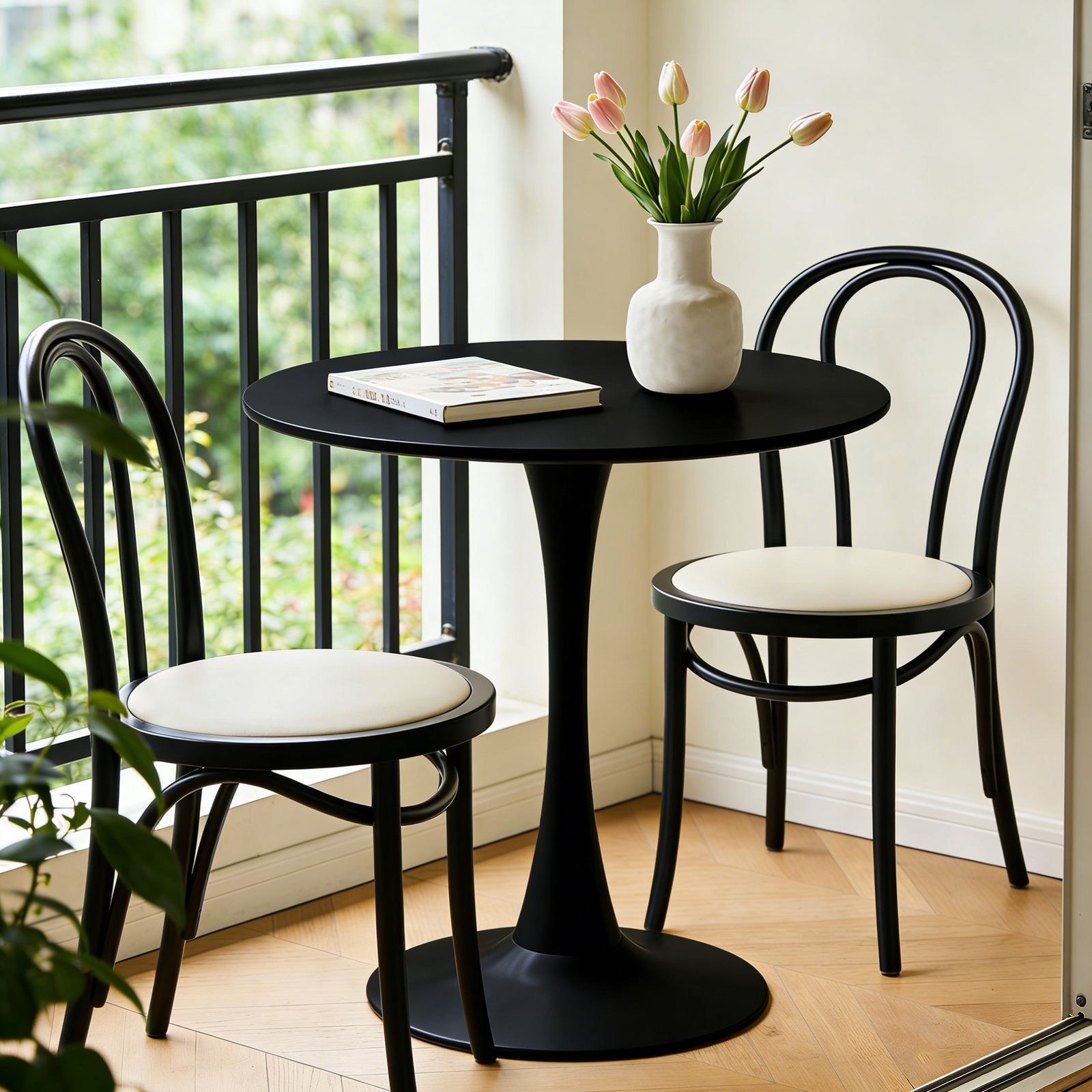 Black round dining table with two black bentwood chairs and tulips on a sunny balcony