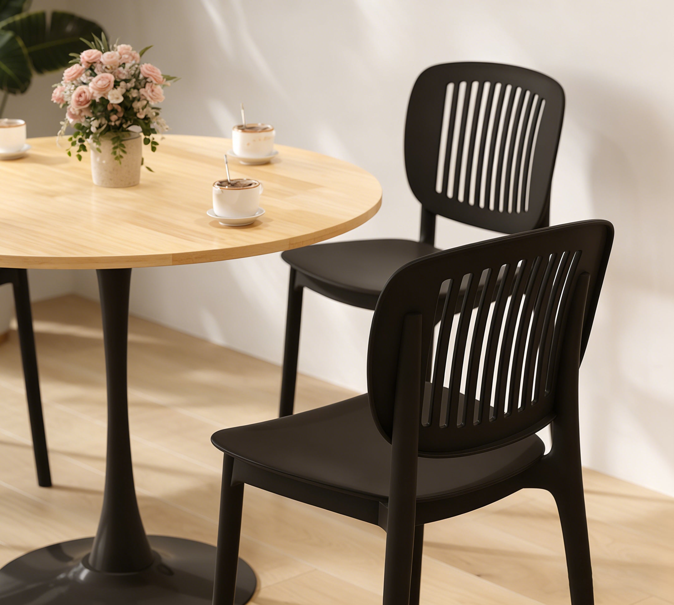 Close-up of the natural round dining table edge with black chairs, coffee cups and pink flowers