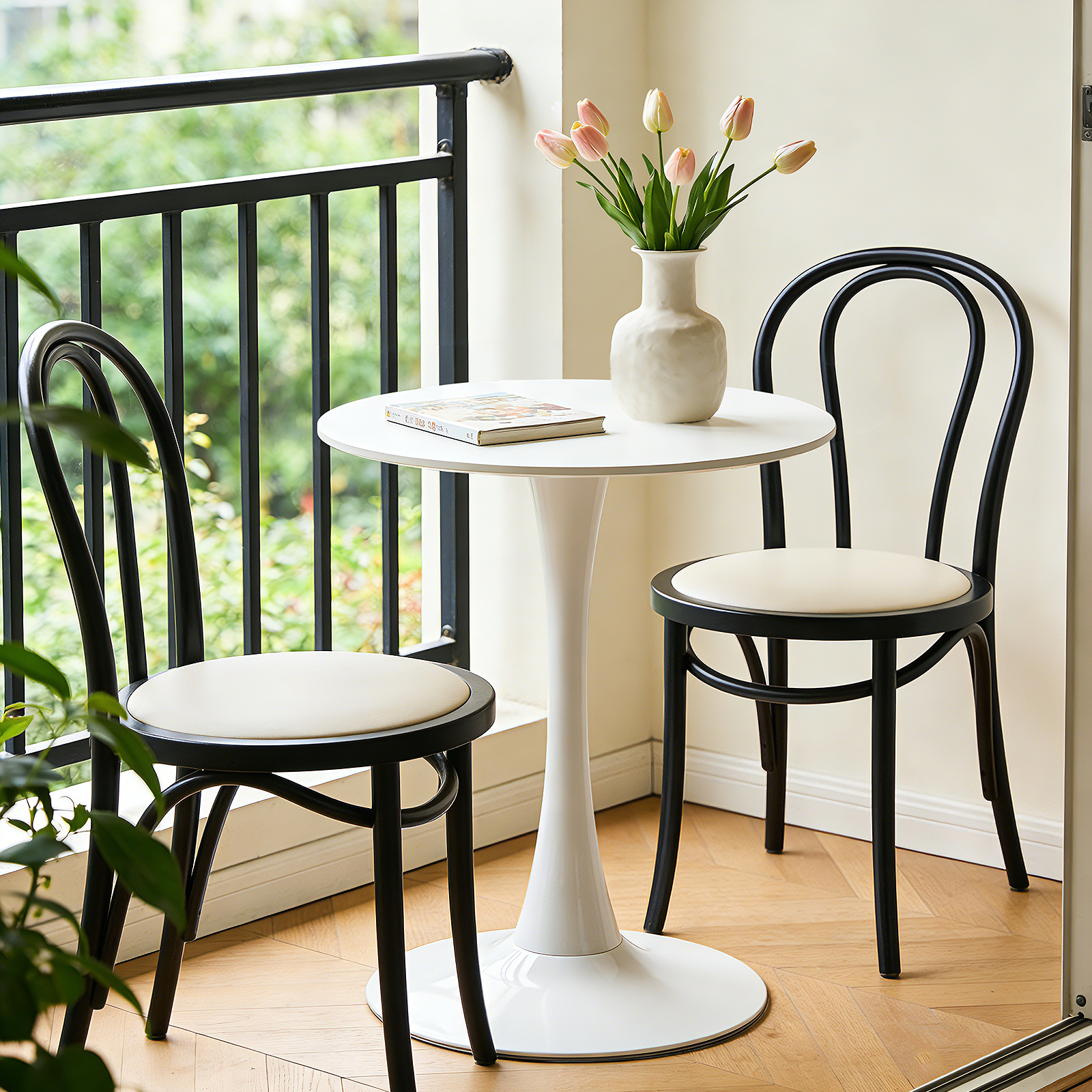 White round tulip bistro table on a balcony with two black bentwood chairs and tulips