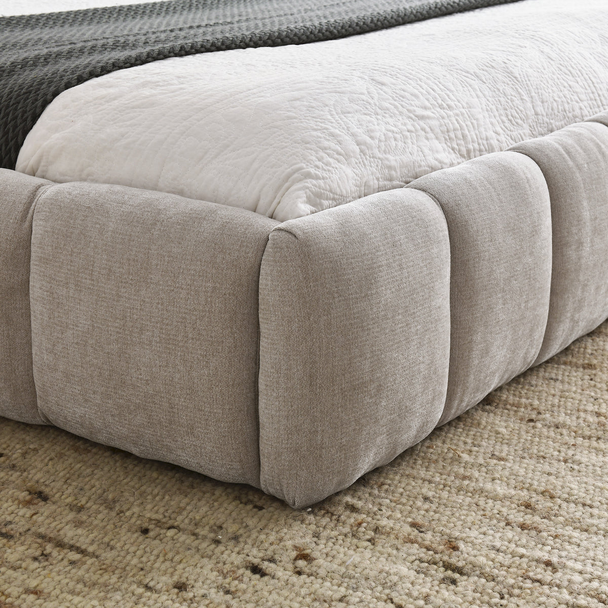 Close-up of the beige chenille bubble-tufted foot rail corner with white bedding
