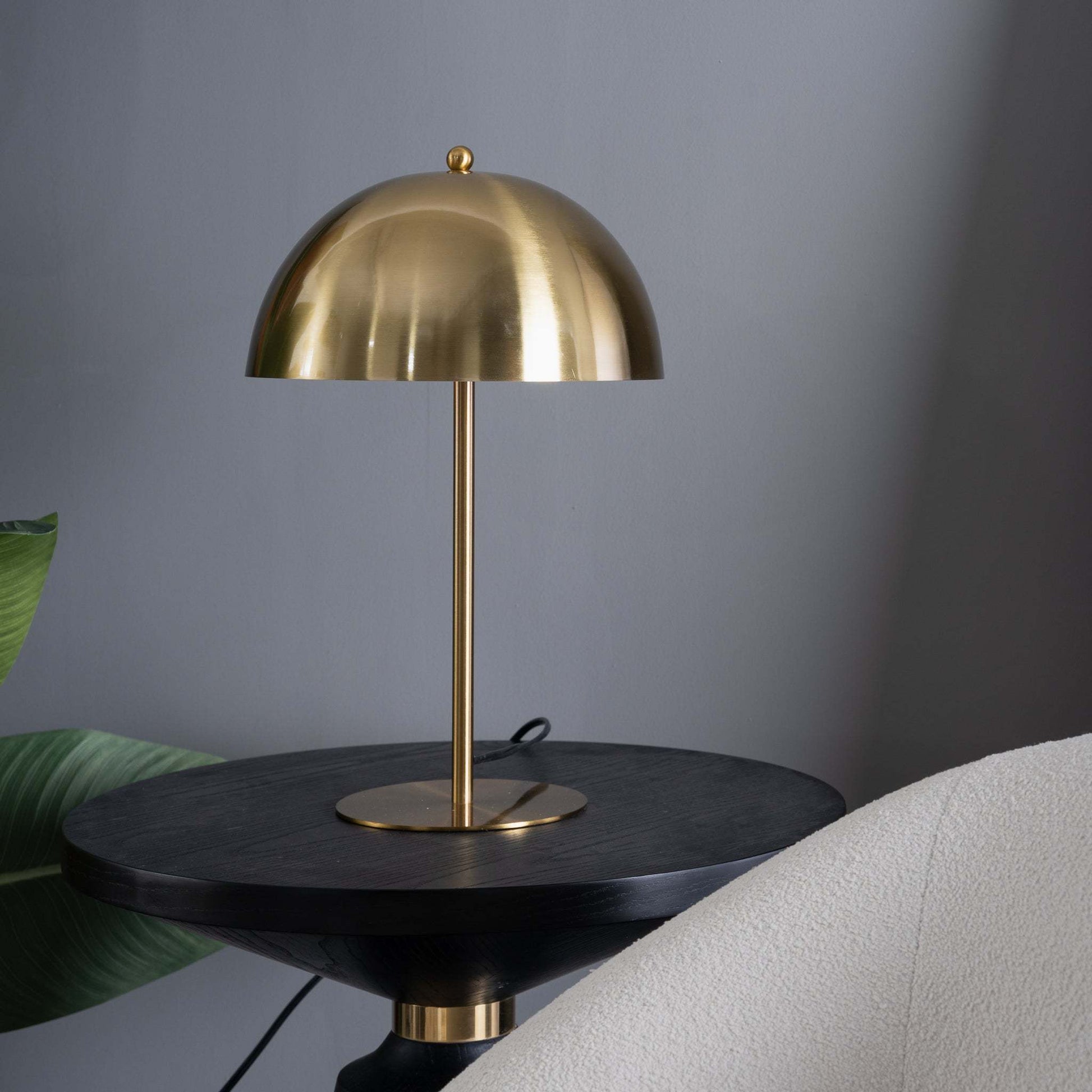 gold dome bedside table lamp sitting on a black end table in a mid century modern apartment