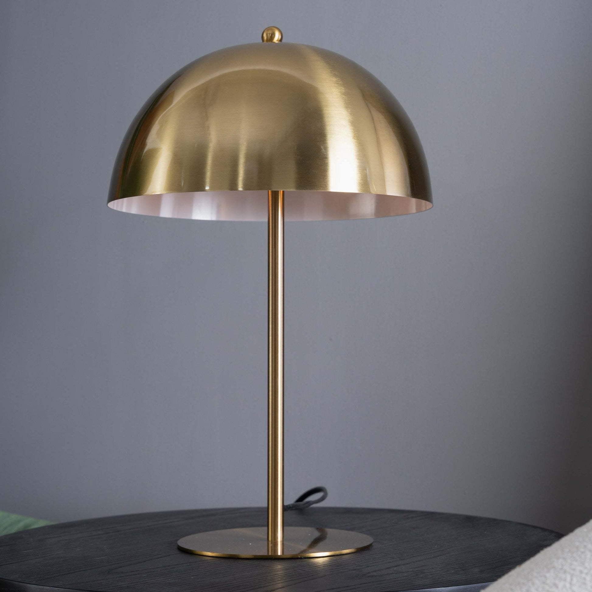 upwards shot of a gold dome table lamp sowing the white ceramic interior of the lampshade sitting on a black wood surface