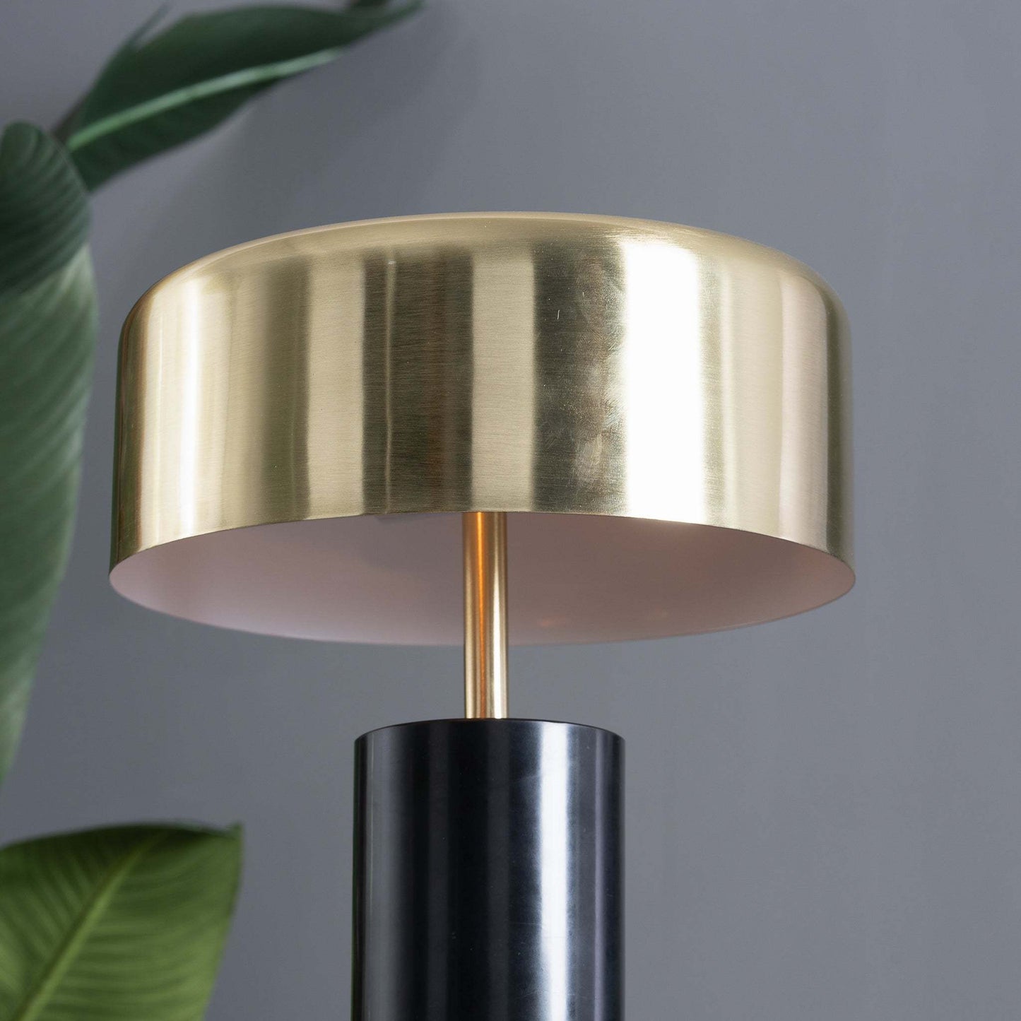close up of gold shade table lamp showing the gold stem black marble base and plants in the background