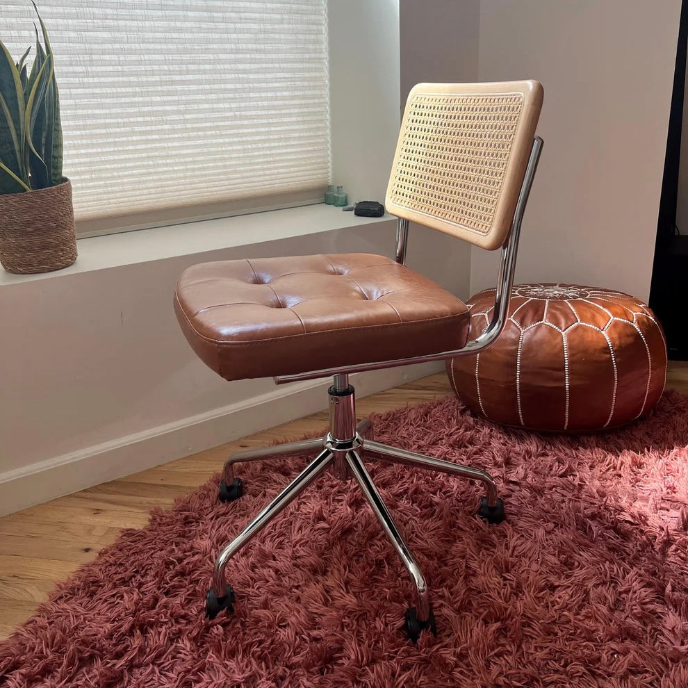 side view of a mid century modern office chair in sunlight with a brown vegan leather seat and a solid wood and rattan back