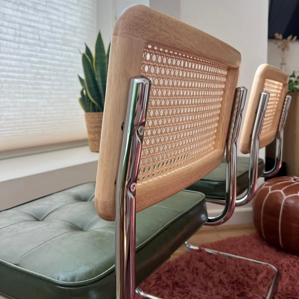 Rearview of stainless steel frame attached to solid wood and natural rattan backrest on green vegan leather dining chair