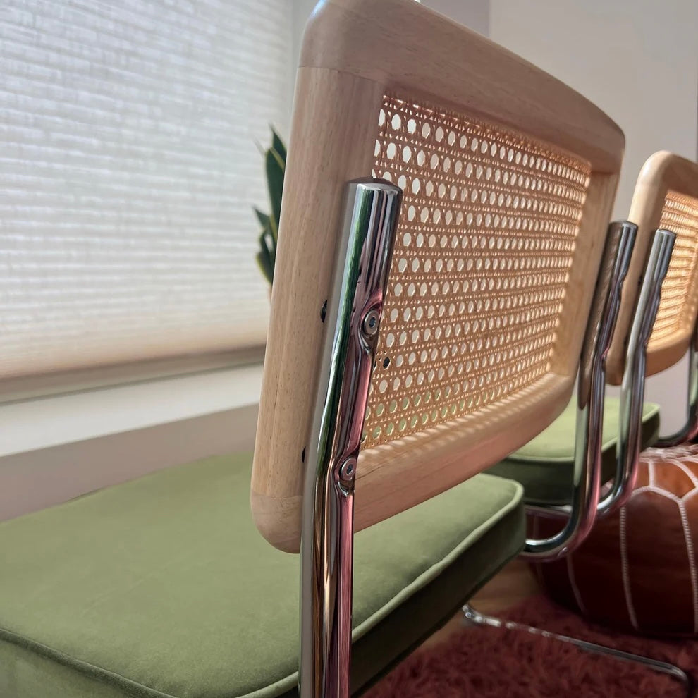 close up of solid wood back rest with rattan accents and a stainless steel frame and a green velvet street