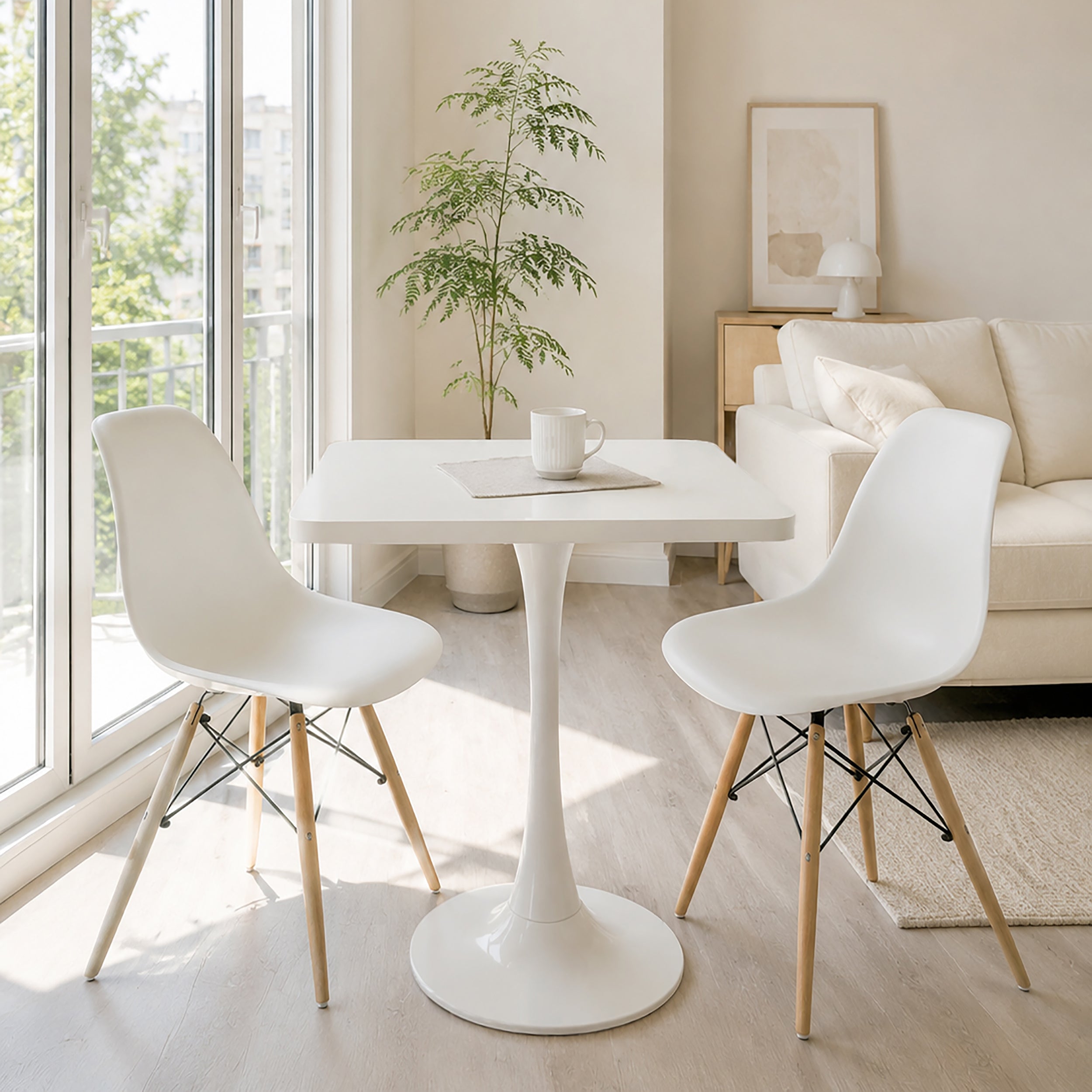 White square tulip bistro table styled in a bright living room with two white molded chairs and a coffee mug