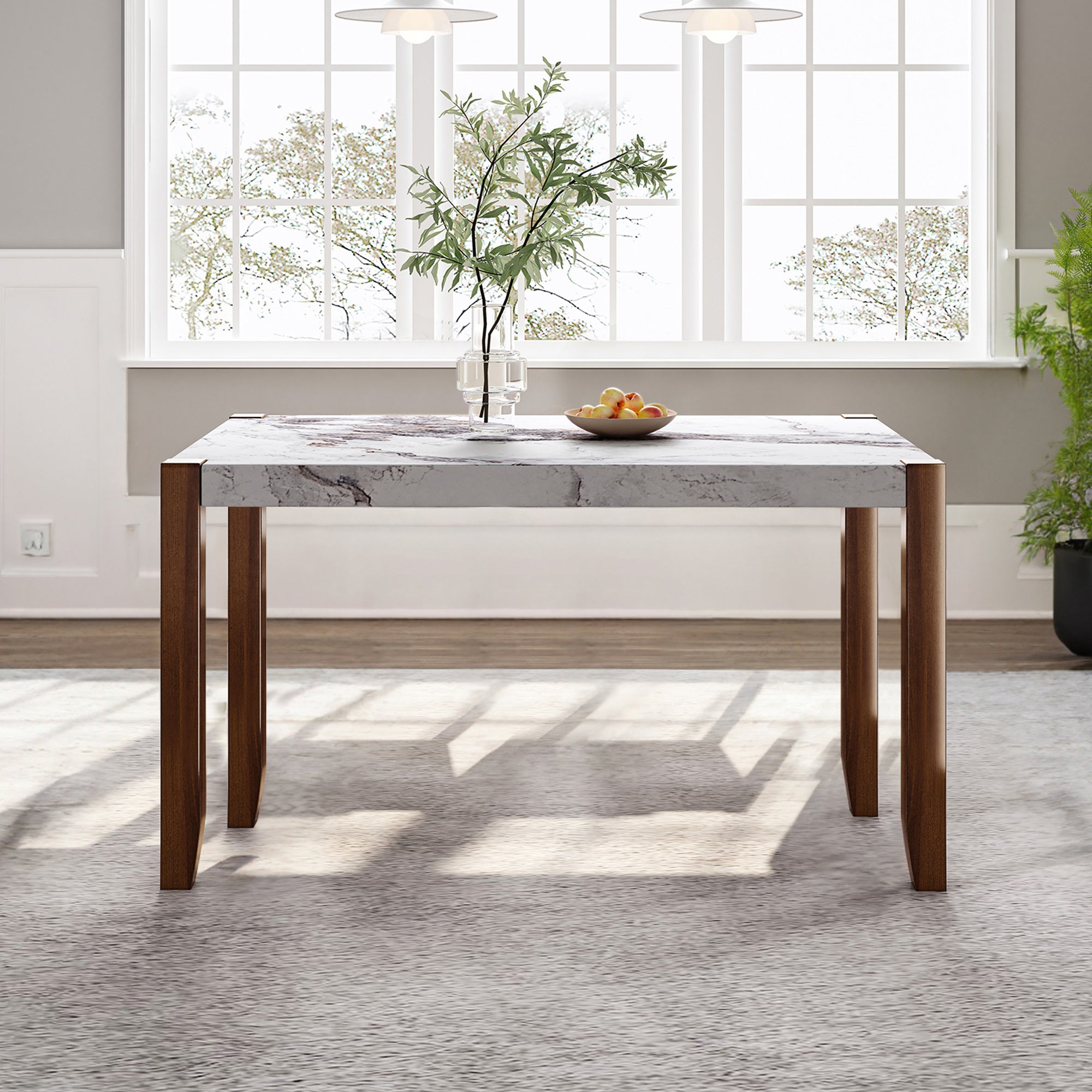 Faux marble dining table with brown wood legs staged by a window with a fruit bowl and vase