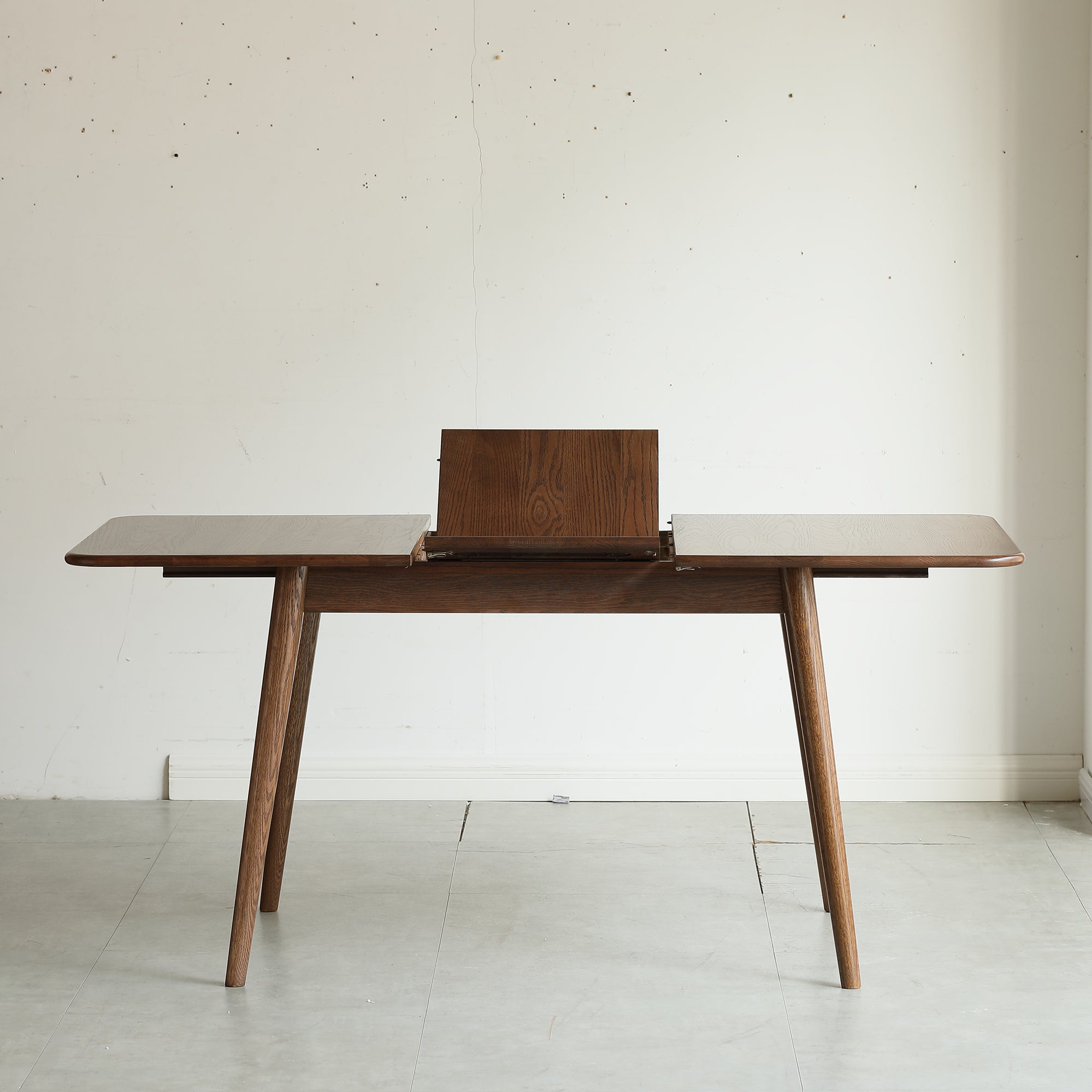 Walnut oak dining table with the center extension leaf folded up mid-extension in a studio