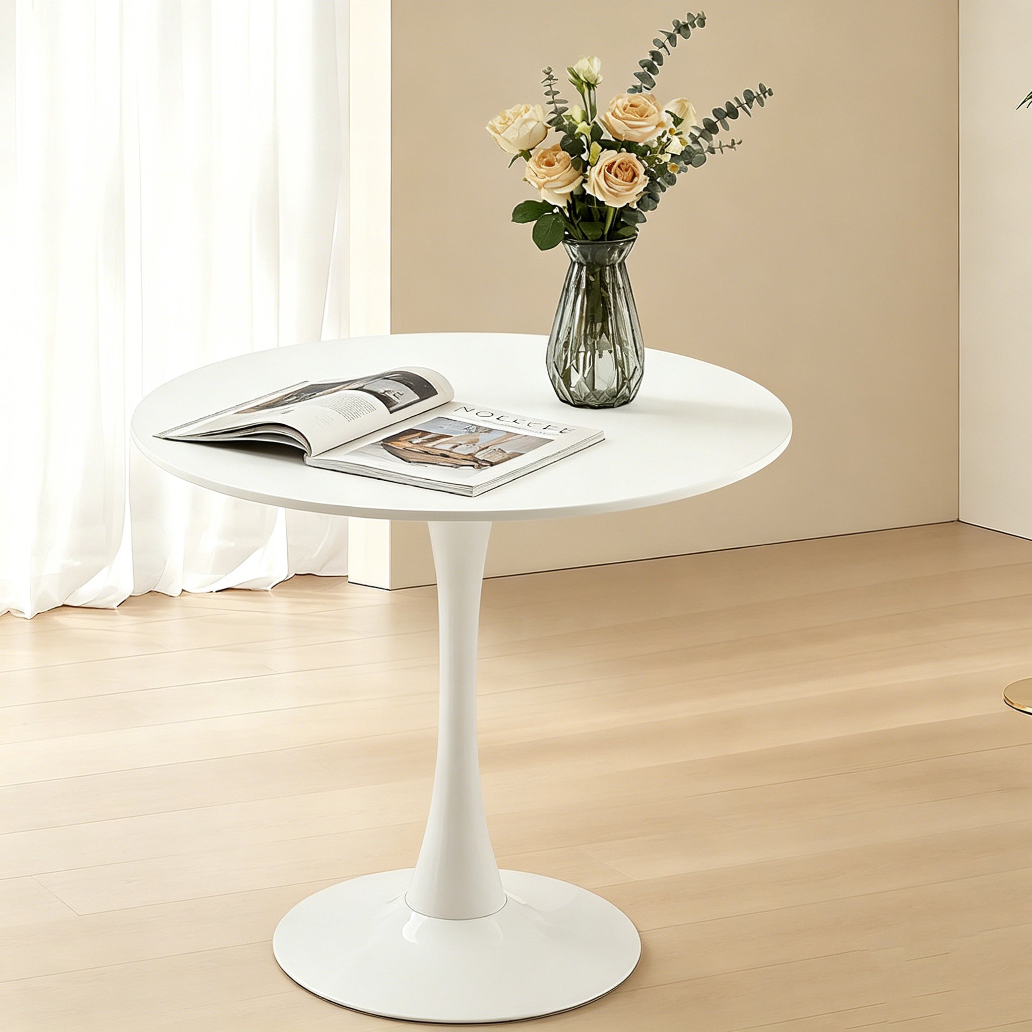 White modern round dining table with tulip pedestal, styled with a magazine and roses by a window