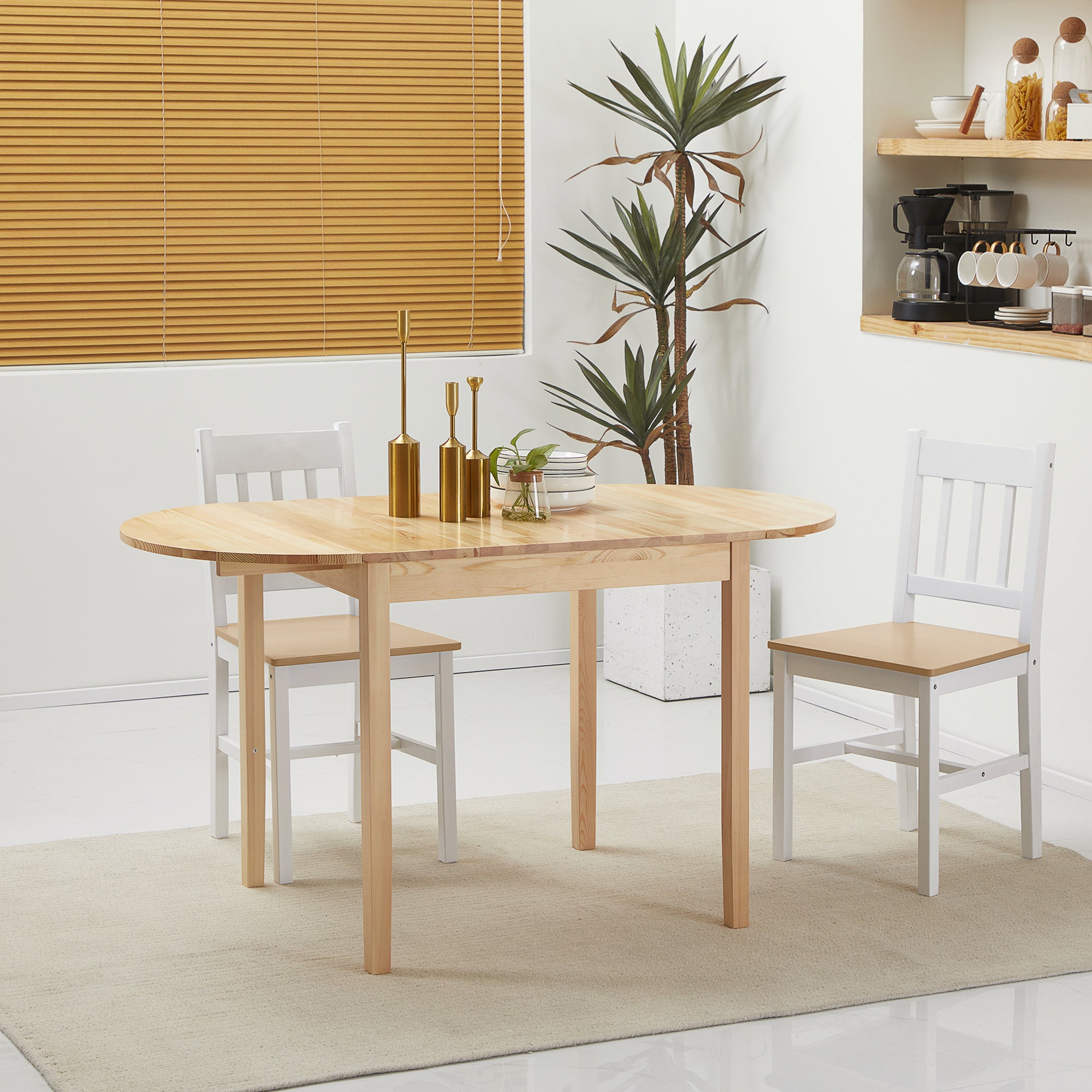 Natural pine drop-leaf table fully extended to an oval, styled in a bright kitchen with two dining chairs