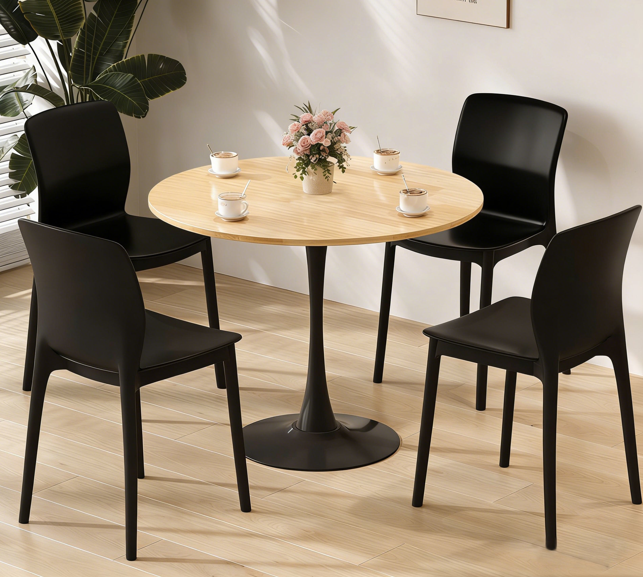 Natural round pedestal dining table set in a room with four black dining chairs, cups and flowers