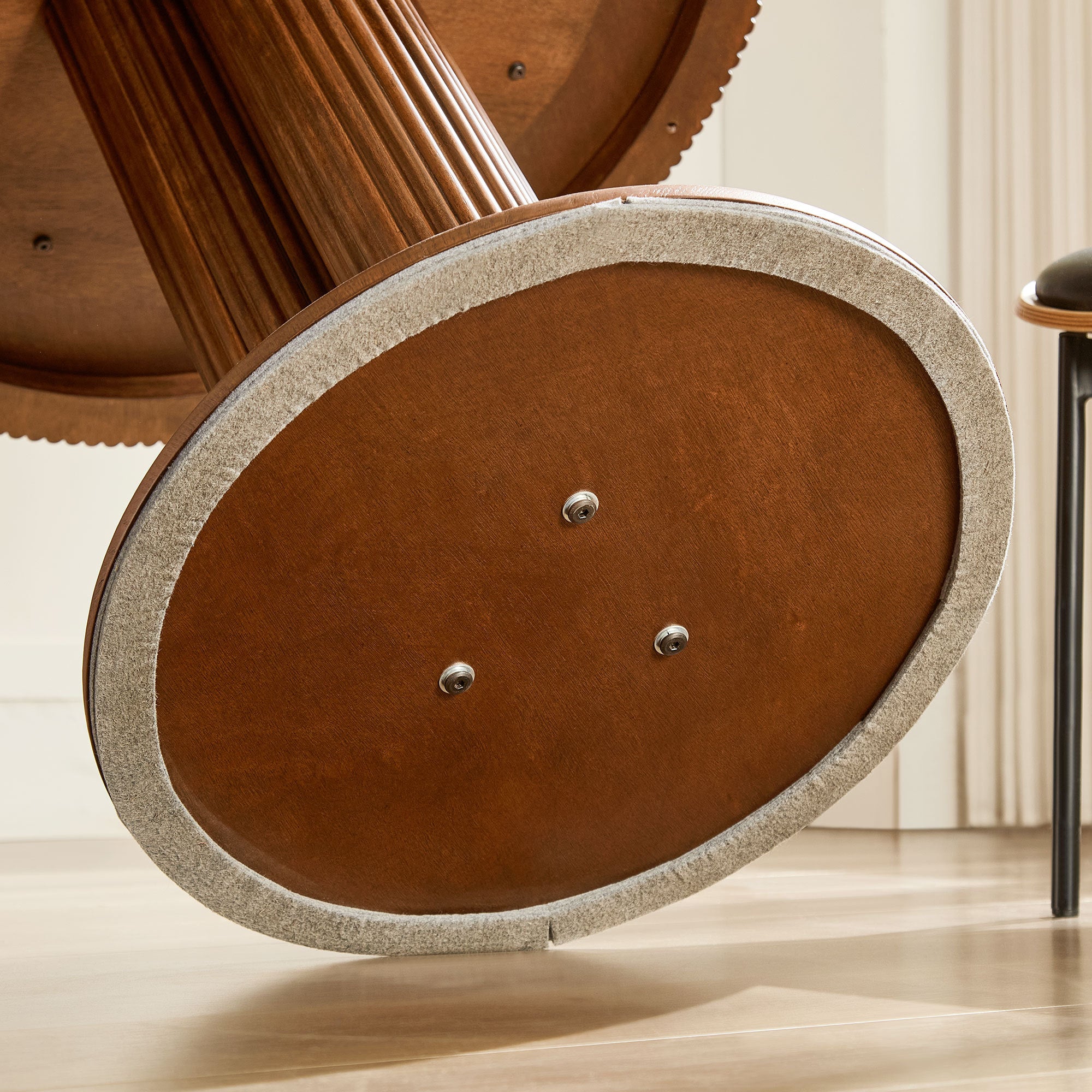 Underside of the round wood base showing a felt pad and three screw fittings