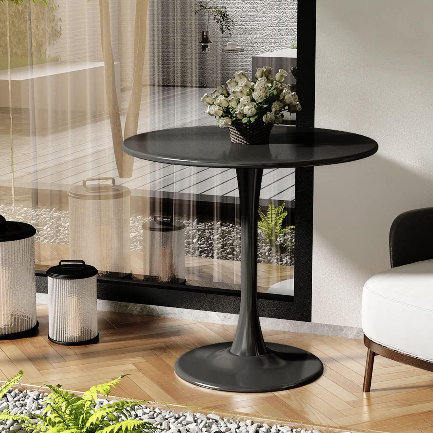 Black round dining table with metal pedestal styled with white roses by a glass wall, three-quarter view