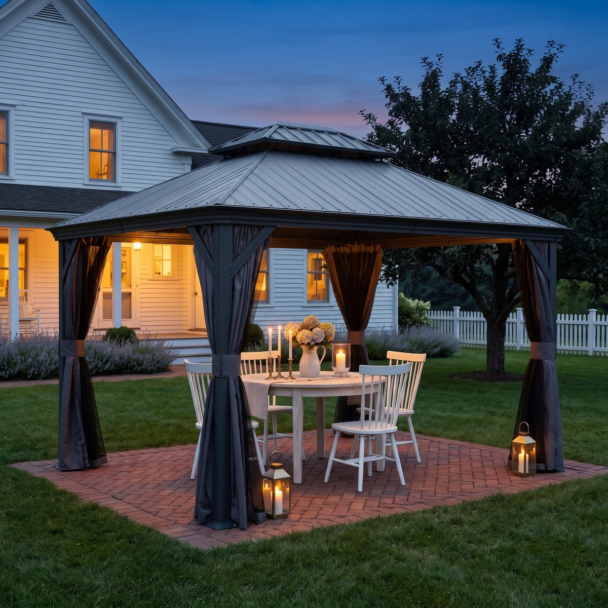 Dark gray double roof hardtop gazebo with tied back curtains over a dining table on a brick patio at dusk