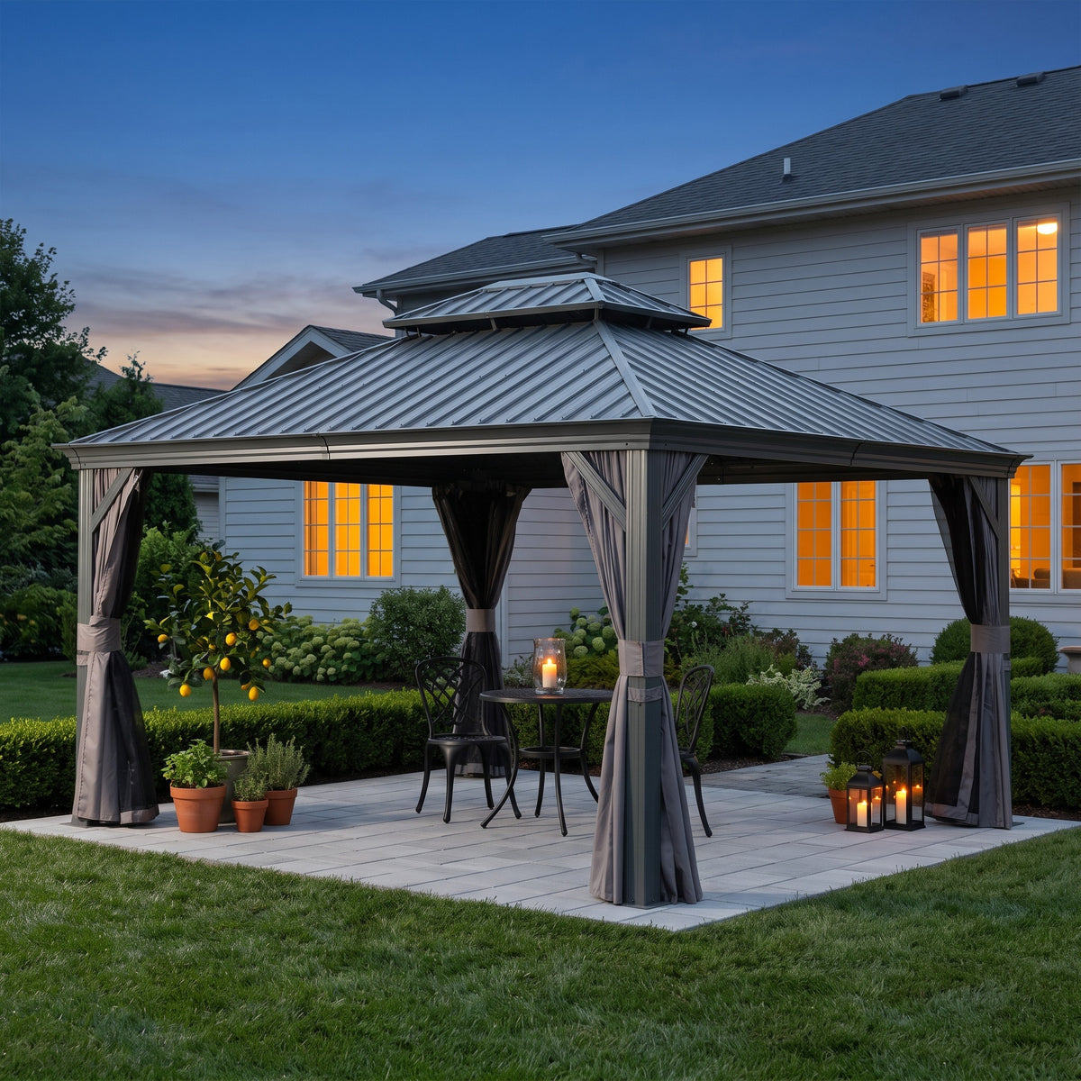 Gray aluminum 10x12 double roof hardtop gazebo with tied back curtains over a bistro set on a stone patio at dusk