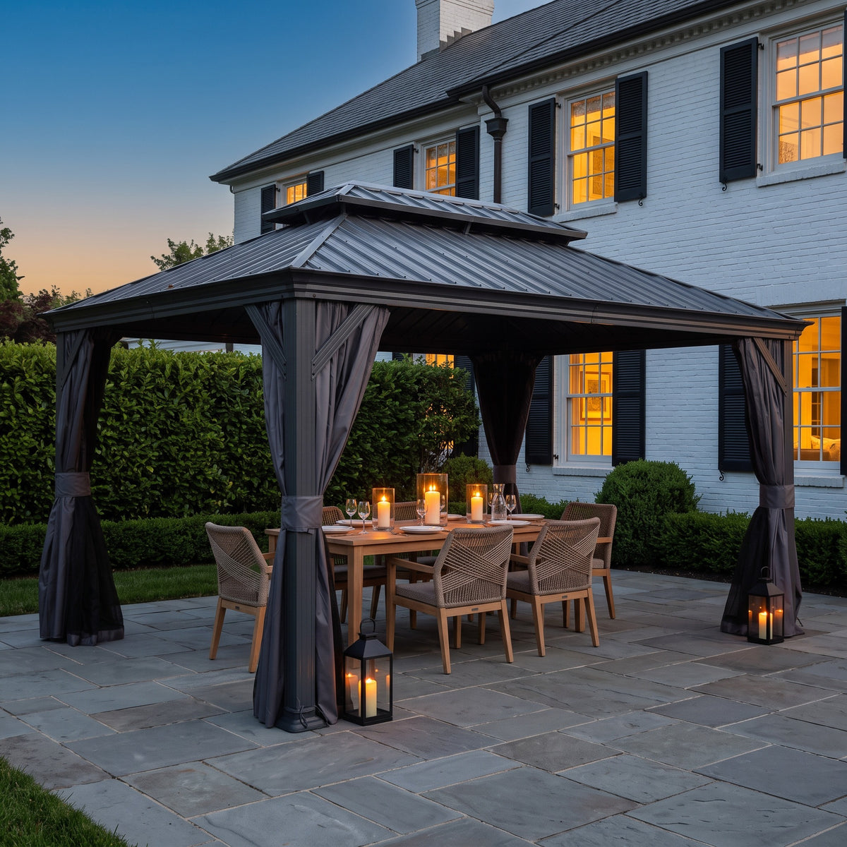 Gray 10x14 hardtop gazebo with tied back curtains over a candlelit dining table on a stone patio at dusk