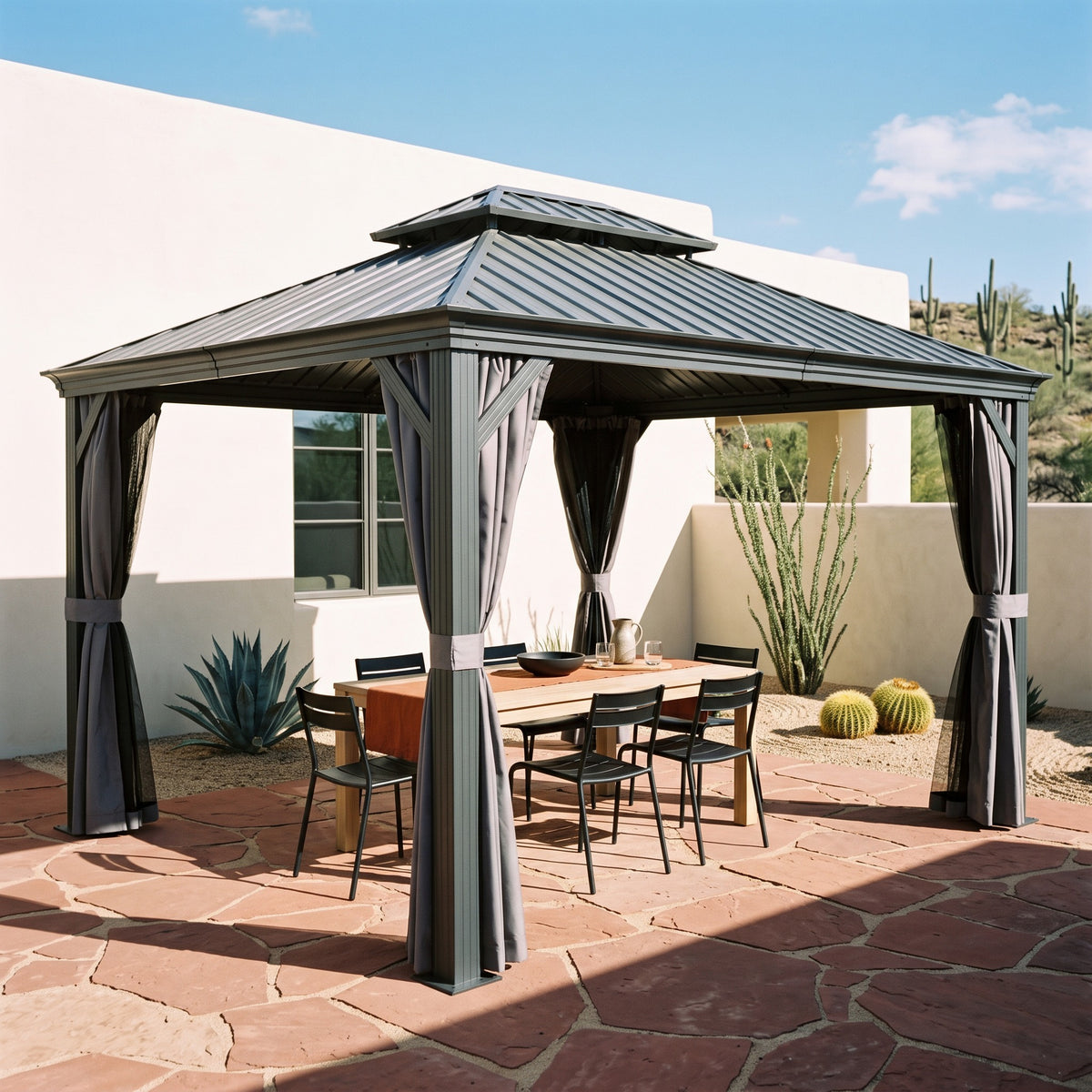 Gray aluminum 12x14 hardtop gazebo with tied back curtains over a dining table on a flagstone patio in desert sun