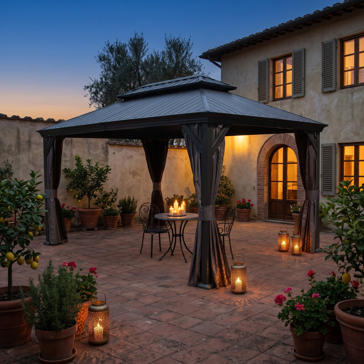 Dark gray double roof hardtop gazebo with tied back curtains over a bistro table in a courtyard at dusk
