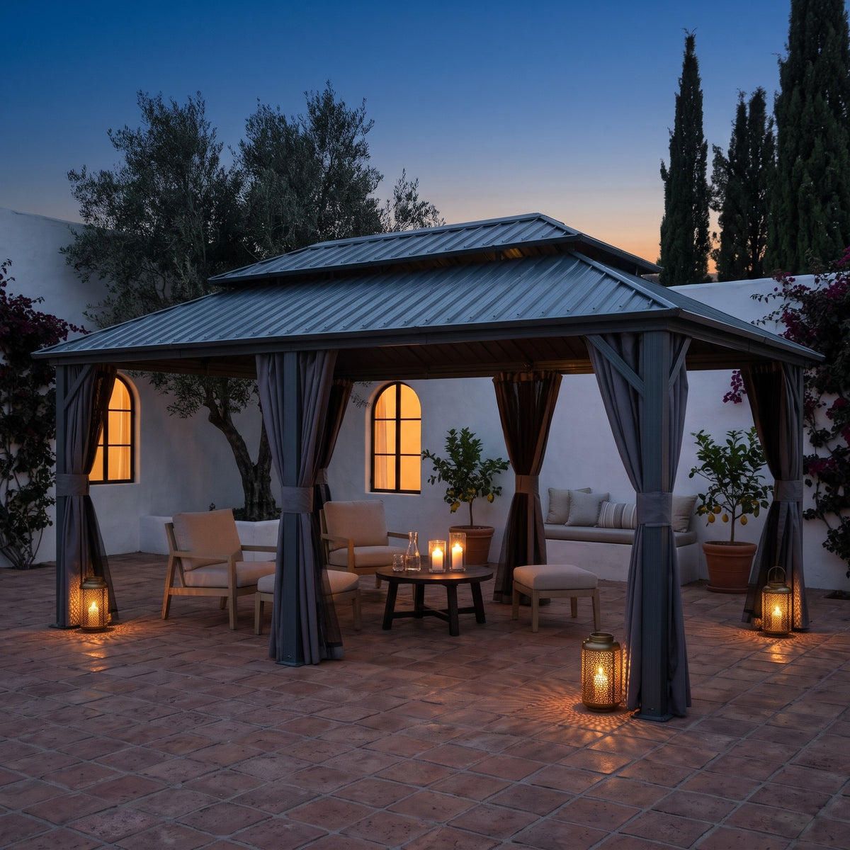 Gray aluminum 12x20 double roof hardtop gazebo with tied back curtains over lounge chairs on a terracotta patio at dusk