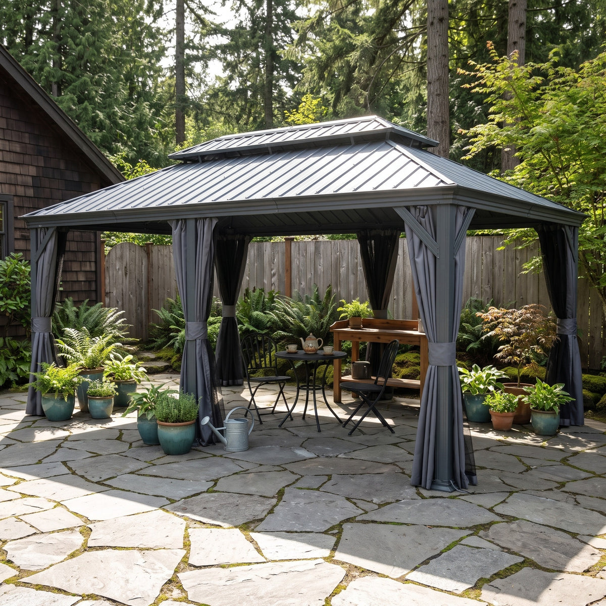 Gray 12x20 hardtop gazebo with tied back curtains over a bistro table on a flagstone patio by a wood fence