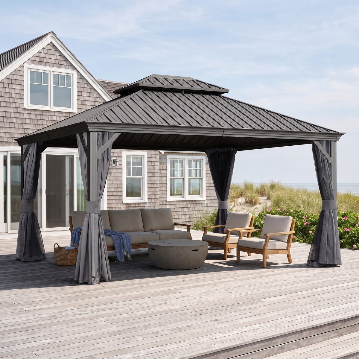 Gray steel double roof hardtop gazebo with tied back curtains over a sofa and lounge chairs on a beach house deck