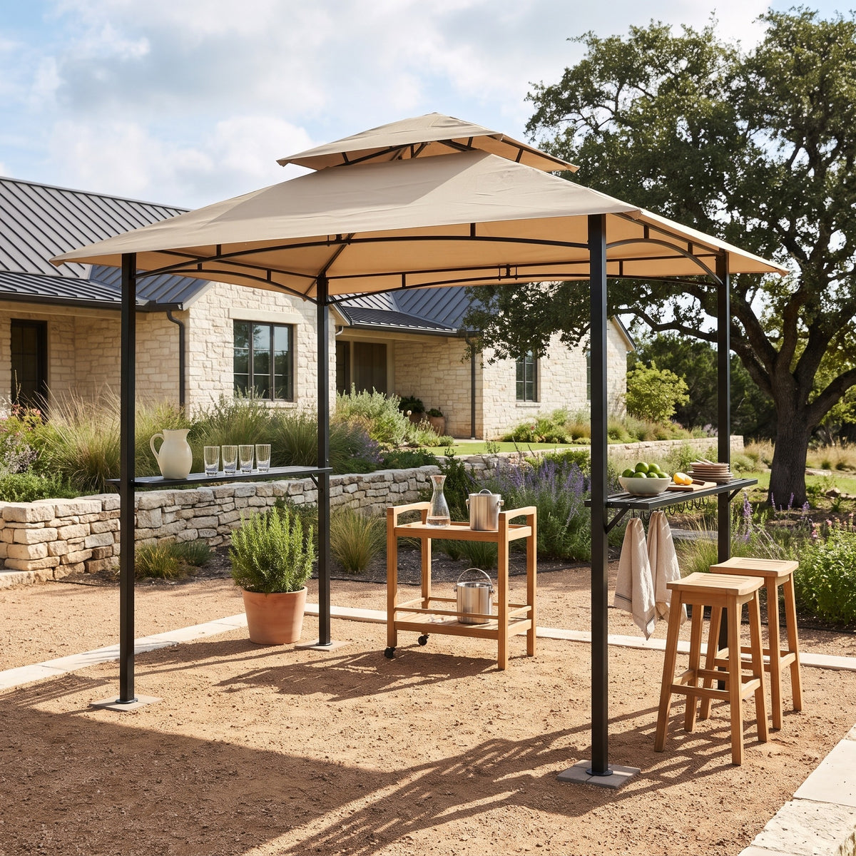 Khaki double roof grill gazebo with black metal posts and side shelves on a gravel patio beside teak stools
