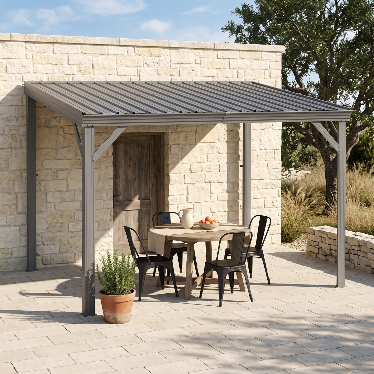 Gray metal lean-to hardtop gazebo against a stone house wall, shading a round table and black chairs on a patio