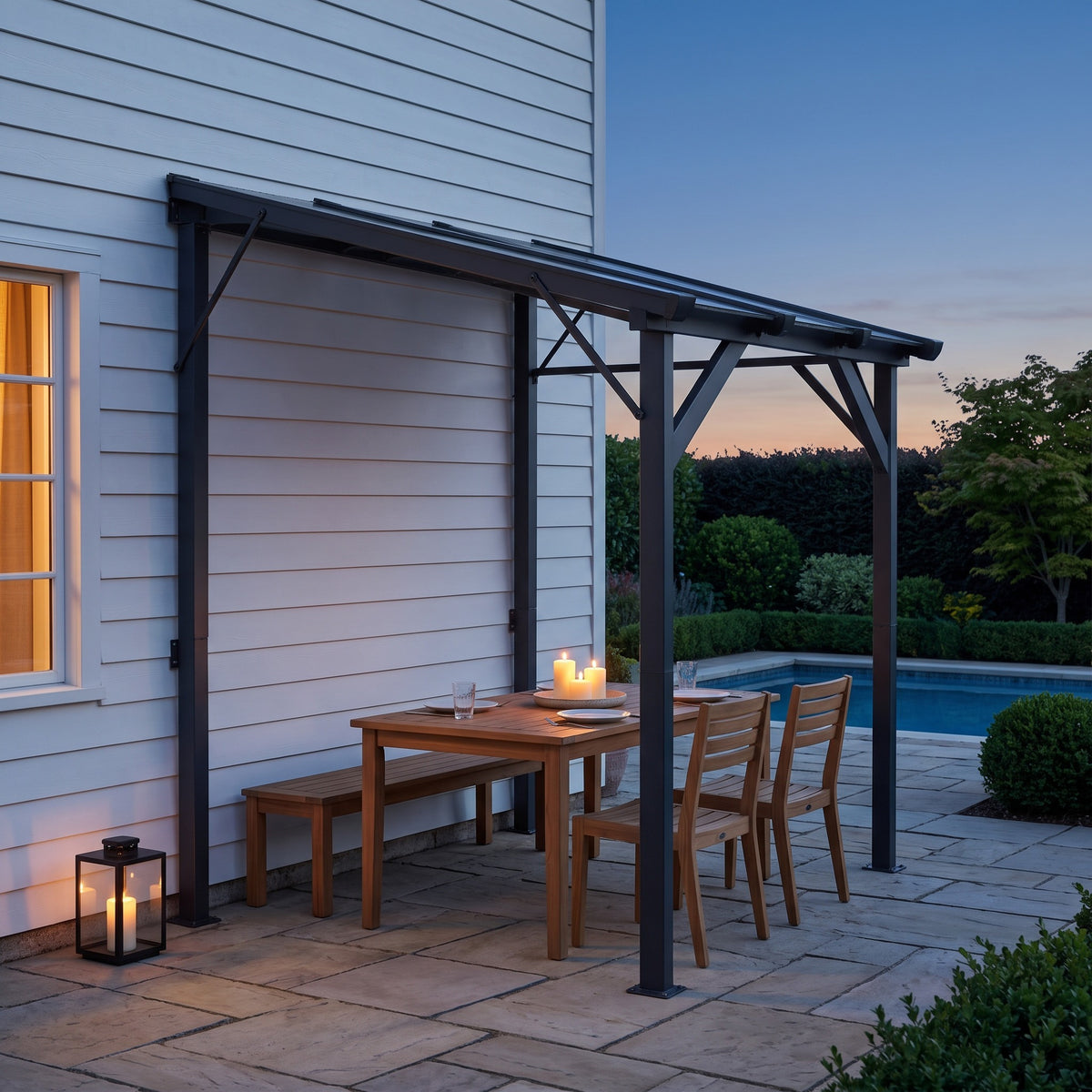 Dark gray metal lean-to hardtop gazebo against a house over a teak dining table with candles at dusk