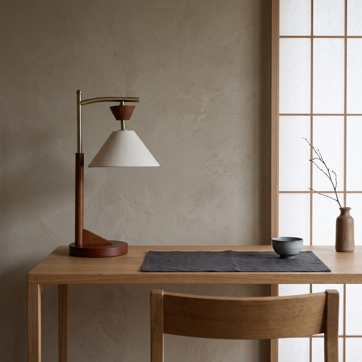 Brown wood table lamp with brass arm and off-white cloth cone shade on an oak desk beside a paper screen