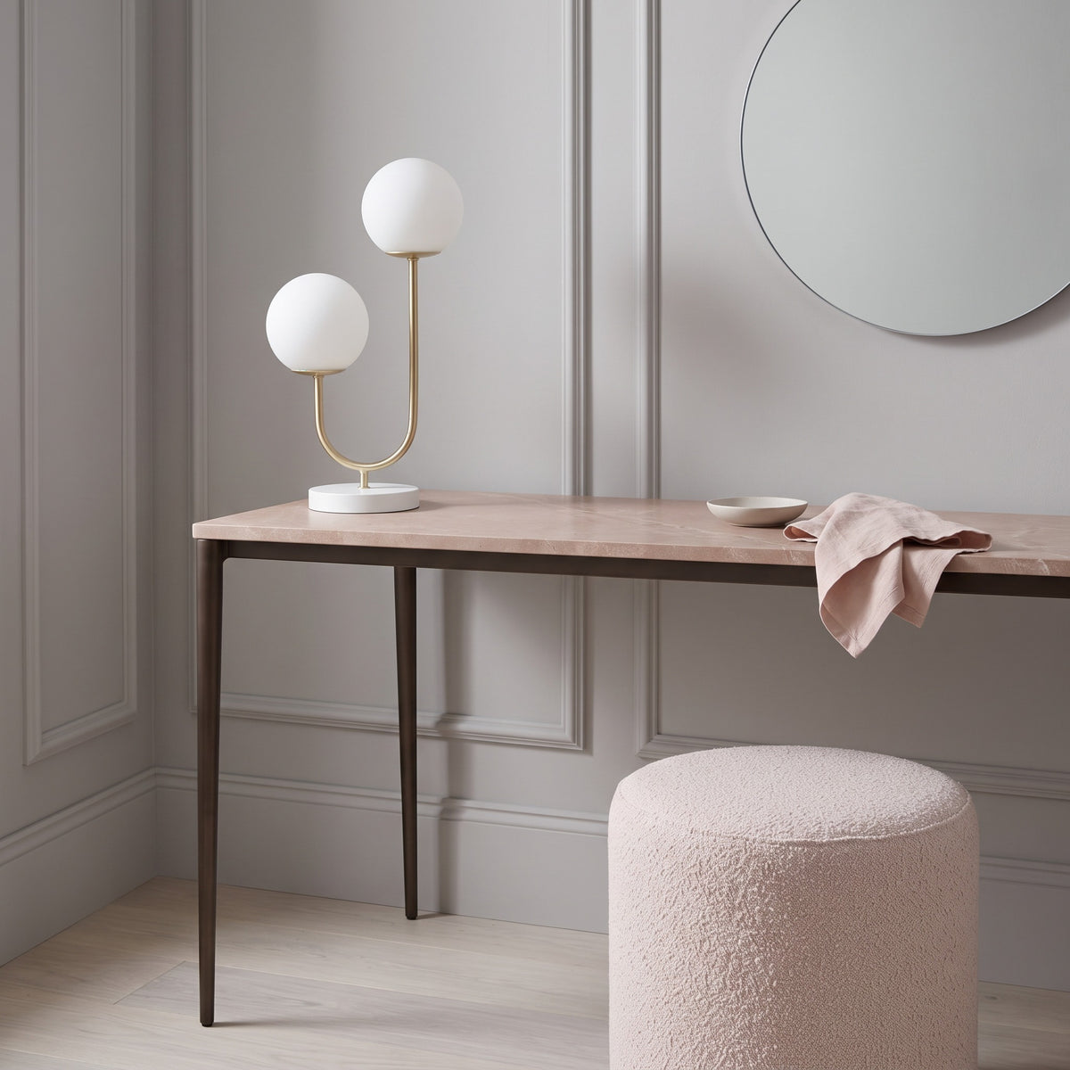 Gold and white table lamp with two frosted glass globes on a blush stone console in a paneled room