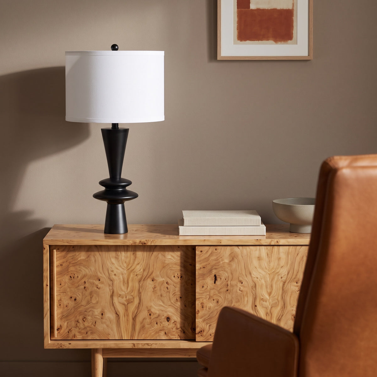 Black table lamp with stacked disc base and white drum shade on a burl wood sideboard