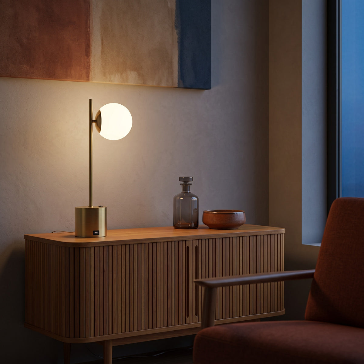 Brass table lamp with lit white glass globe shade on a fluted wood console at dusk