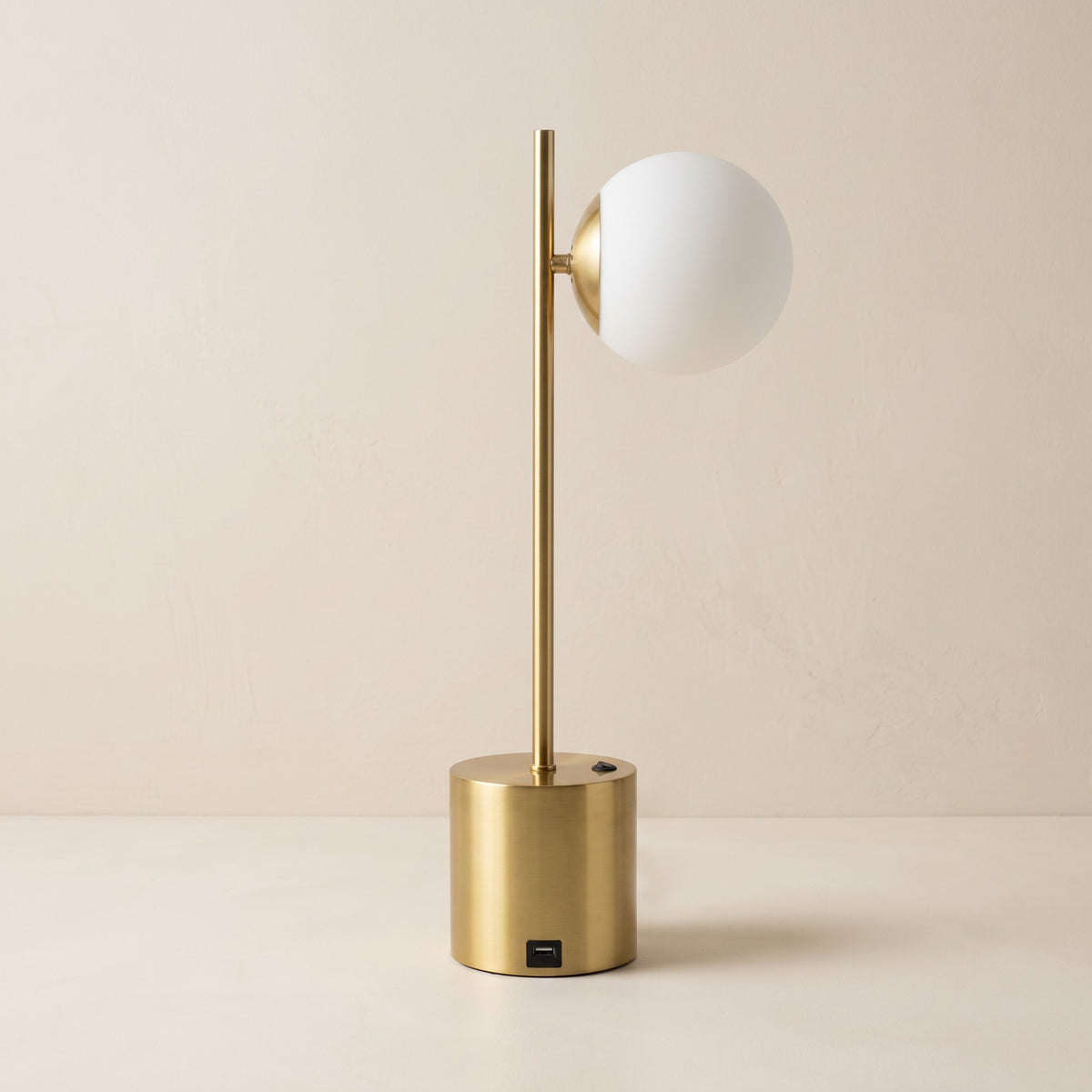 Brass table lamp with white glass globe shade and round base on an ivory plaster backdrop