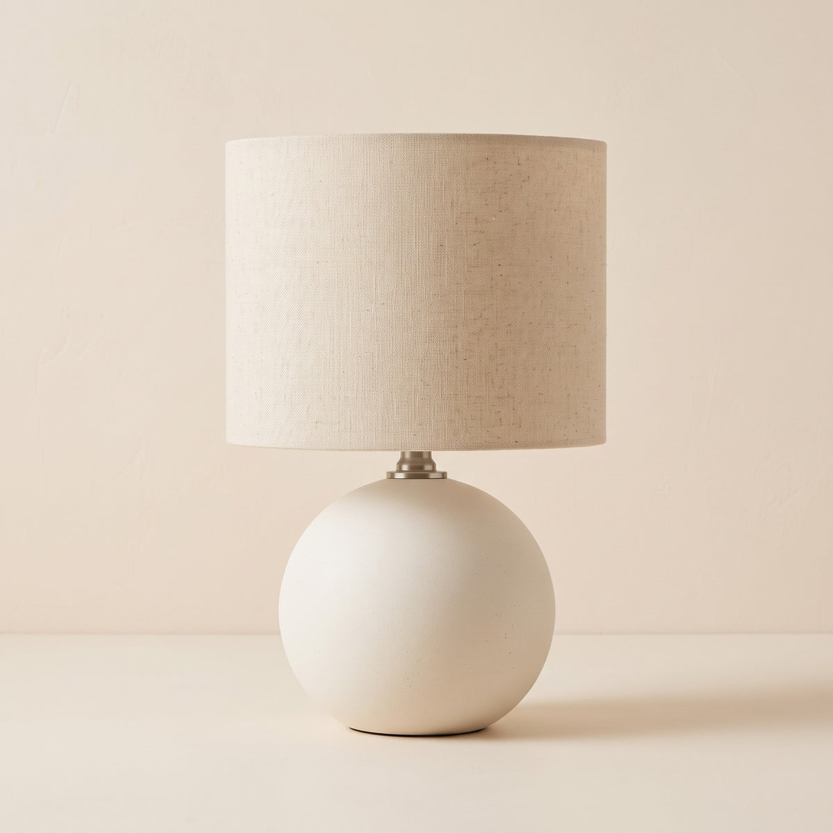 Cream ceramic globe table lamp with linen-look drum shade on an ivory plaster backdrop