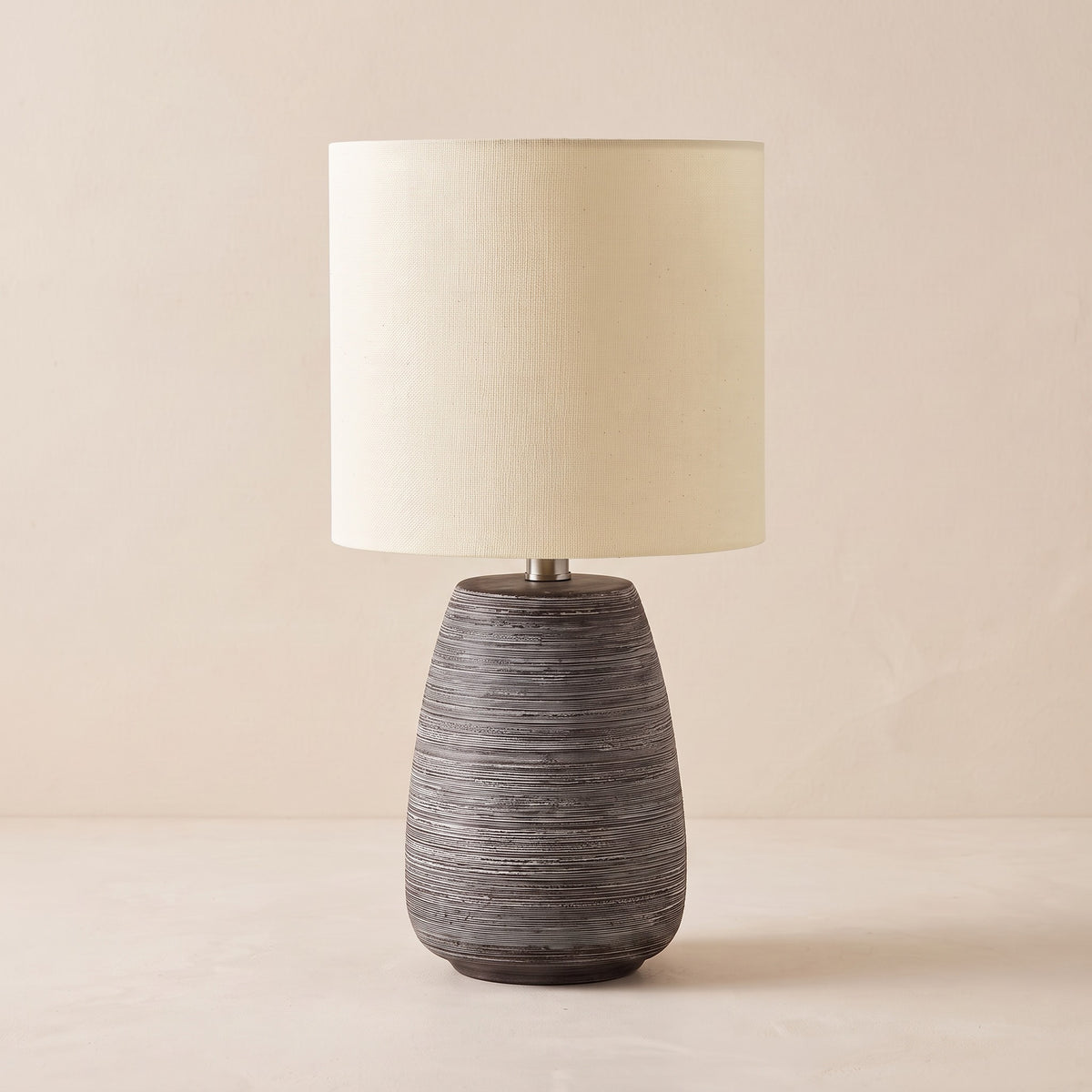 Grey ribbed ceramic table lamp with ivory linen-look drum shade on a warm off-white backdrop