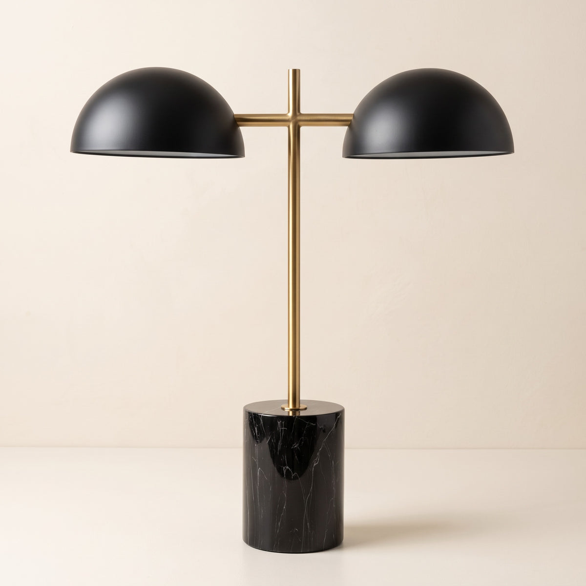 Black marble-look table lamp with two black dome shades on a brass finish stem against an ivory plaster wall