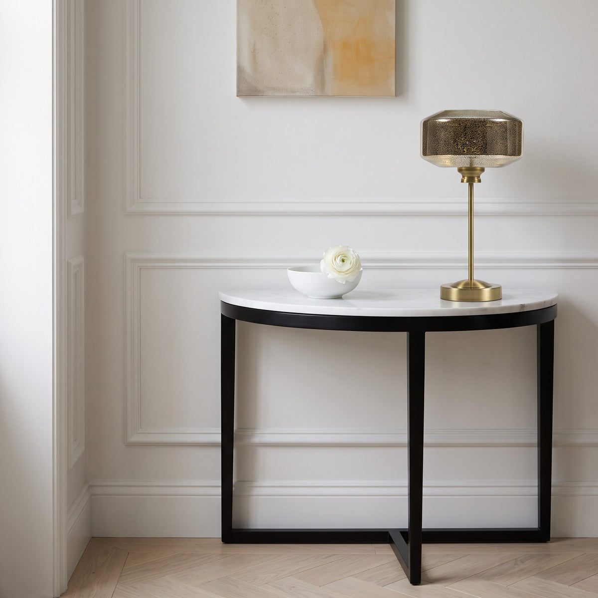 Gold table lamp with smoked mercury glass shade on a white marble demilune console in a white panelled hallway
